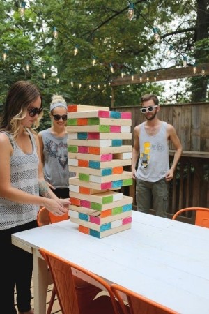 A group of three people playing a Jenga-like game with larger pieces of wood in a backyard. 