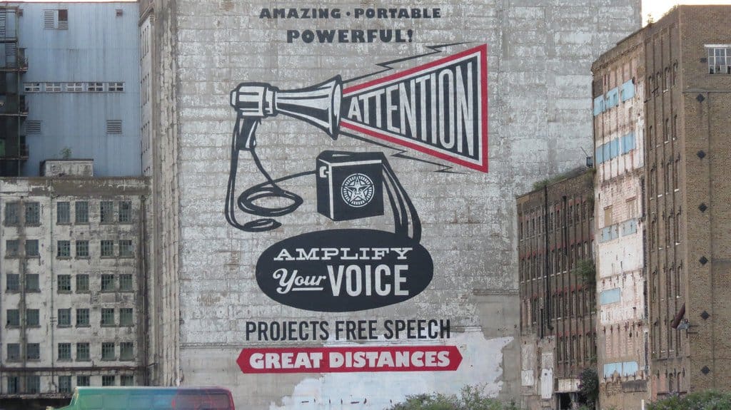 A building with a painted ad. An illustration of a megaphone with the text: Amazing, portable, powerful. Amplify your voice. Projects free speech great distances. 