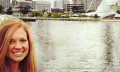 A photograph of Ariel Steeber in front of a body of water with a city behind it. 