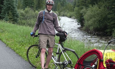 A photograph of Keith Hagen next to a bike on a road next to a river. 