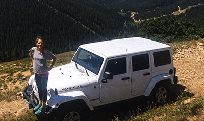 A photograph of Mandy Mangold Wall standing on a Jeep Rubicon on a mountain dirt road.