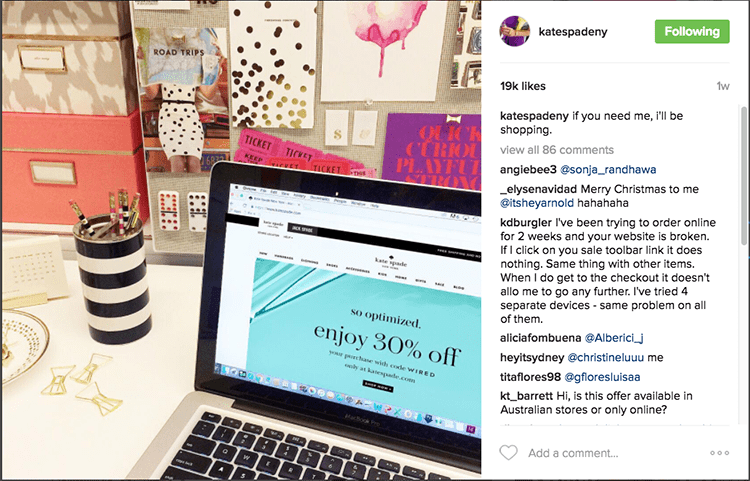 Kate spade Instagram desktop post. A photograph of a desk with a laptop displaying a Kate Spade sale. Next to the laptop is a pencil holder and gold bow paperclips. 