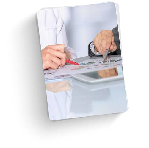 A photograph of two people sitting at a table and pointing with pens at a report. 