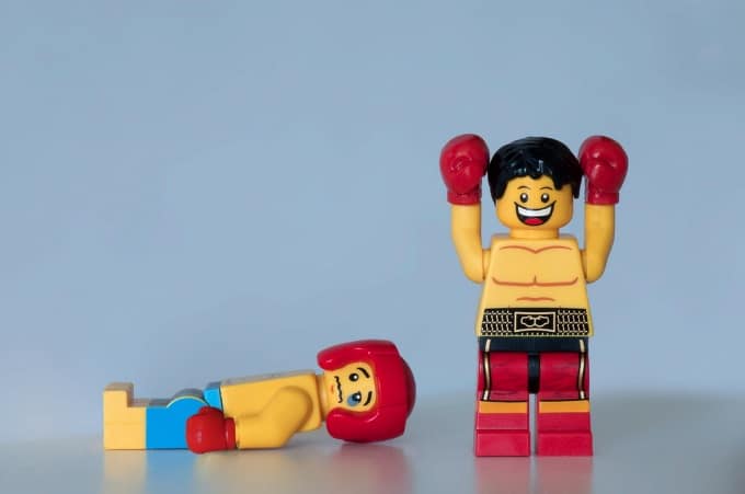 A photograph of two Lego boxers, one raising hands in victory after knocking out the other.