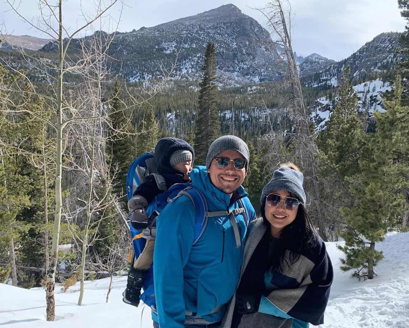 A photograph of Cesar Tellez with his wife and young child in a carrier on his back. In the background are mountains and snow.