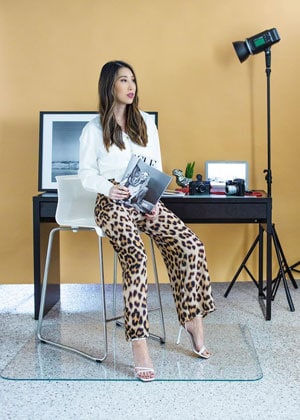 A photograph of Chris Han sitting on a chair on a glass chair mat with a desk behind her. 