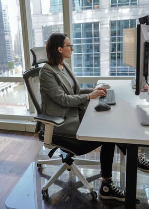 A photograph of MorganCodes sitting at a desk in an office using a glass chair mat. 