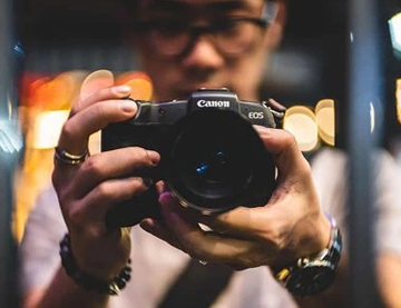 A photograph of a man holding a Canon camera in front of him. 