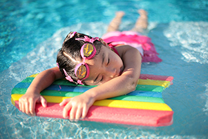 A photograph of a young girl resting her upper body on a float in a pool. 