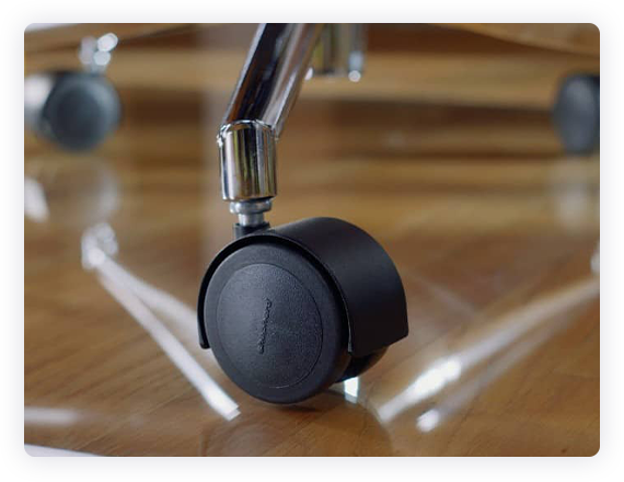 A close up photograph of the wheel of a chair on a glass chair mat. 