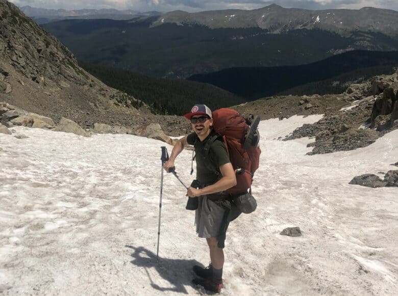 Jeremiah backpacks on a trail in the Rocky Mountains, with a view of the mountains in the background.