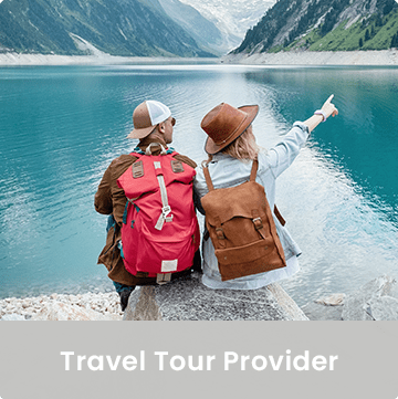 Photo of two people sitting on a rock in front of a lake. One is pointing to the distance. Caption: Travel Tour Provider.