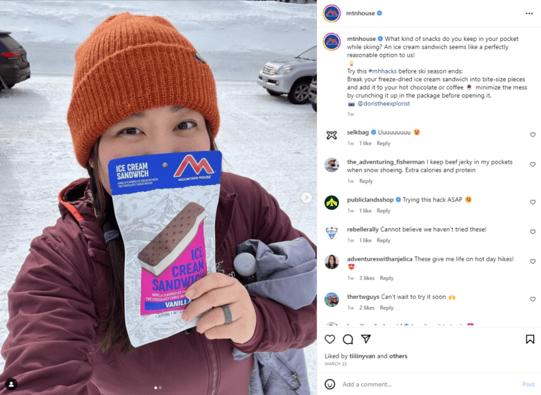 Mountain House Instagram post. Photo: An Asian woman holds a Mountain House ice cream sandwich bag in front of her face in the ski lodge parking lot. Caption: What kind of snacks do you keep in your pocket while skiing? An ice cream sandwich seems like a perfectly reasonable option to us!