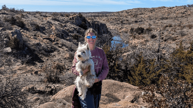 Aimee Heck holds her dog, Yeti, in front of a desert landscape.